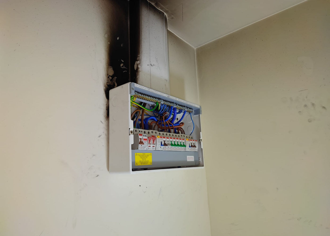 Consumer unit on a wall with smoke damage from a previous electrical fault above it